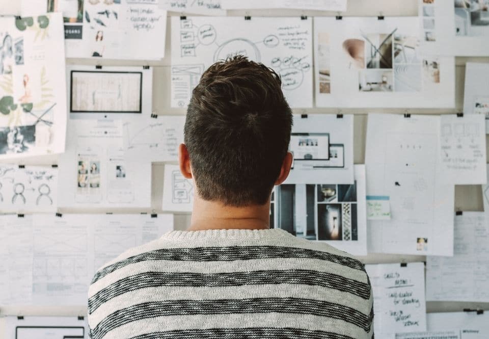man standing in front of a pin board of notes and plans