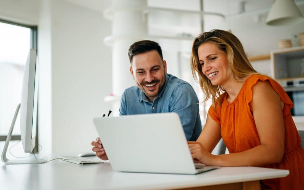 A man with glasses looking at a laptop, sat opposite on the other side of a desk is a woman